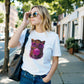 Woman wearing a white t-shirt with a colorful cat graphic, standing on a sidewalk.