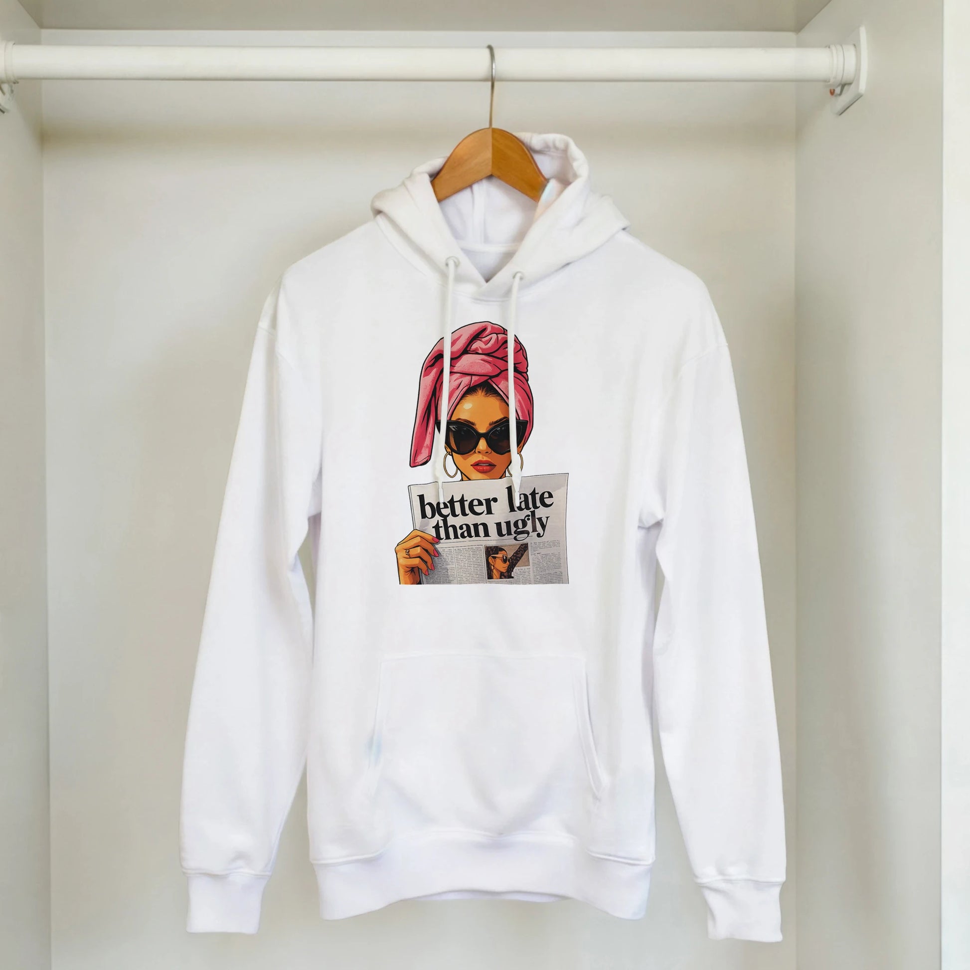 White hoodie with graphic design of a woman with a pink turban and sunglasses, with text 'better late than ugly' on a hanger.
