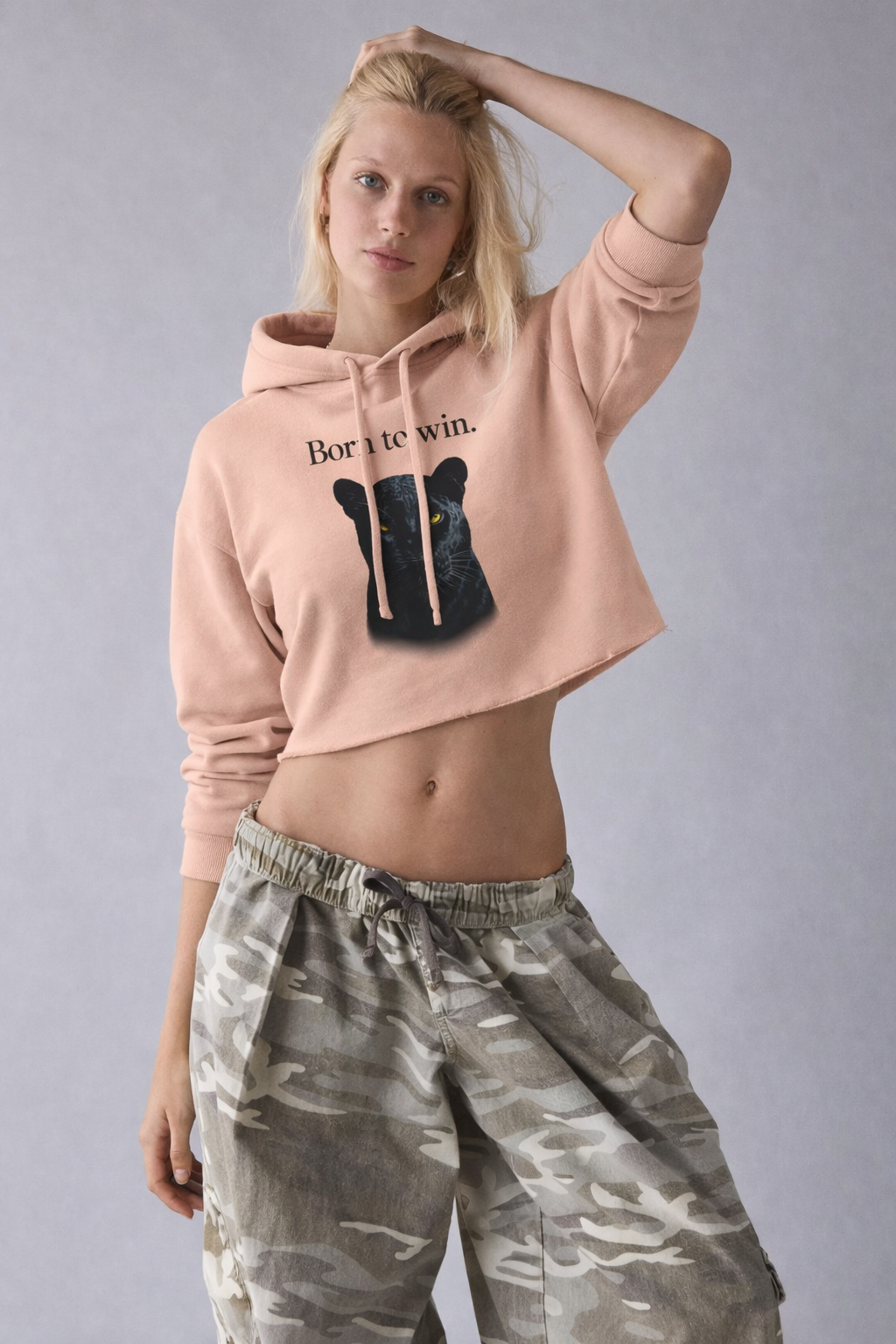 Woman wearing a pink hoodie with text and a graphic, paired with camouflage pants on a gray background