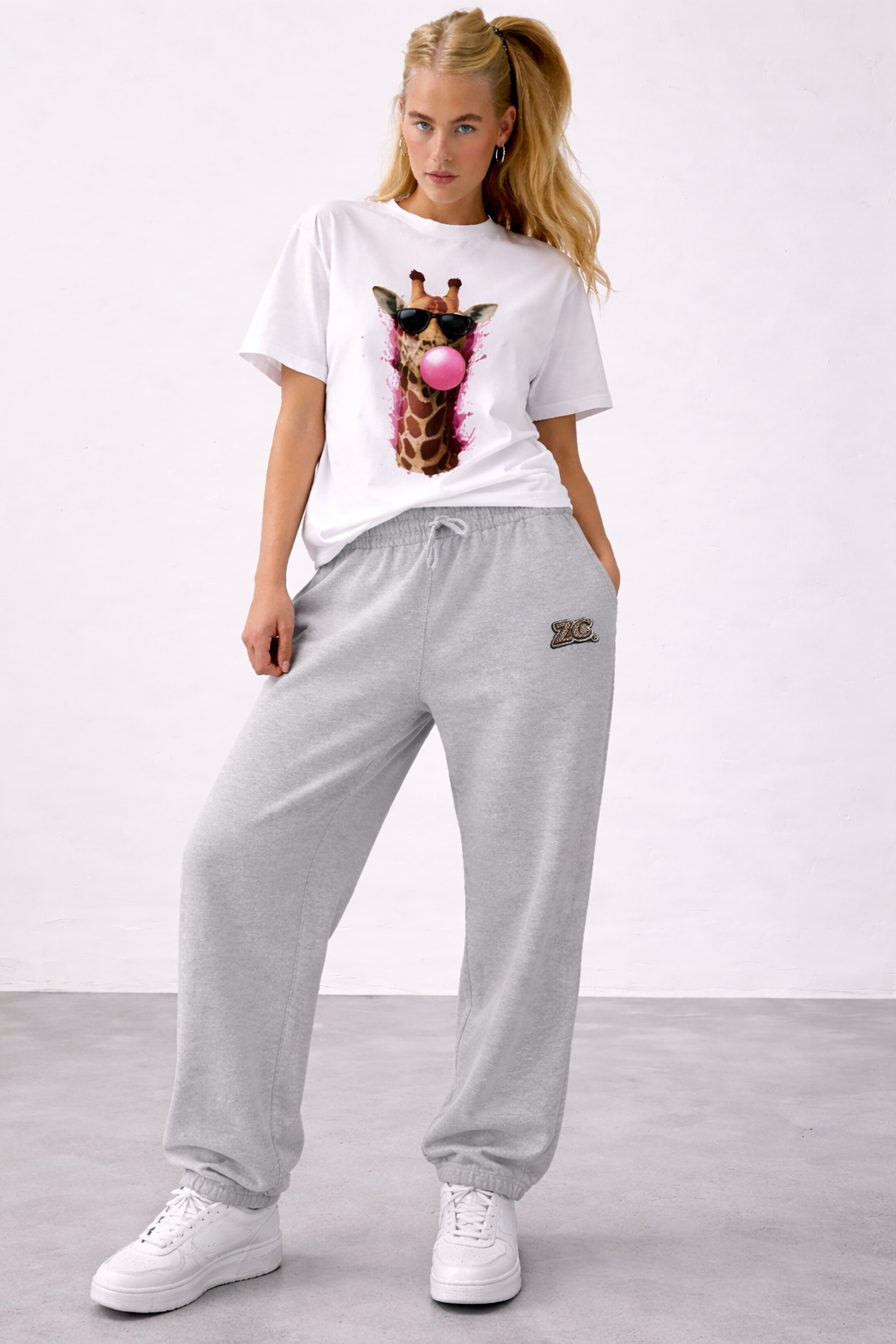 Woman wearing a white t-shirt with a giraffe graphic and gray sweatpants on a plain background