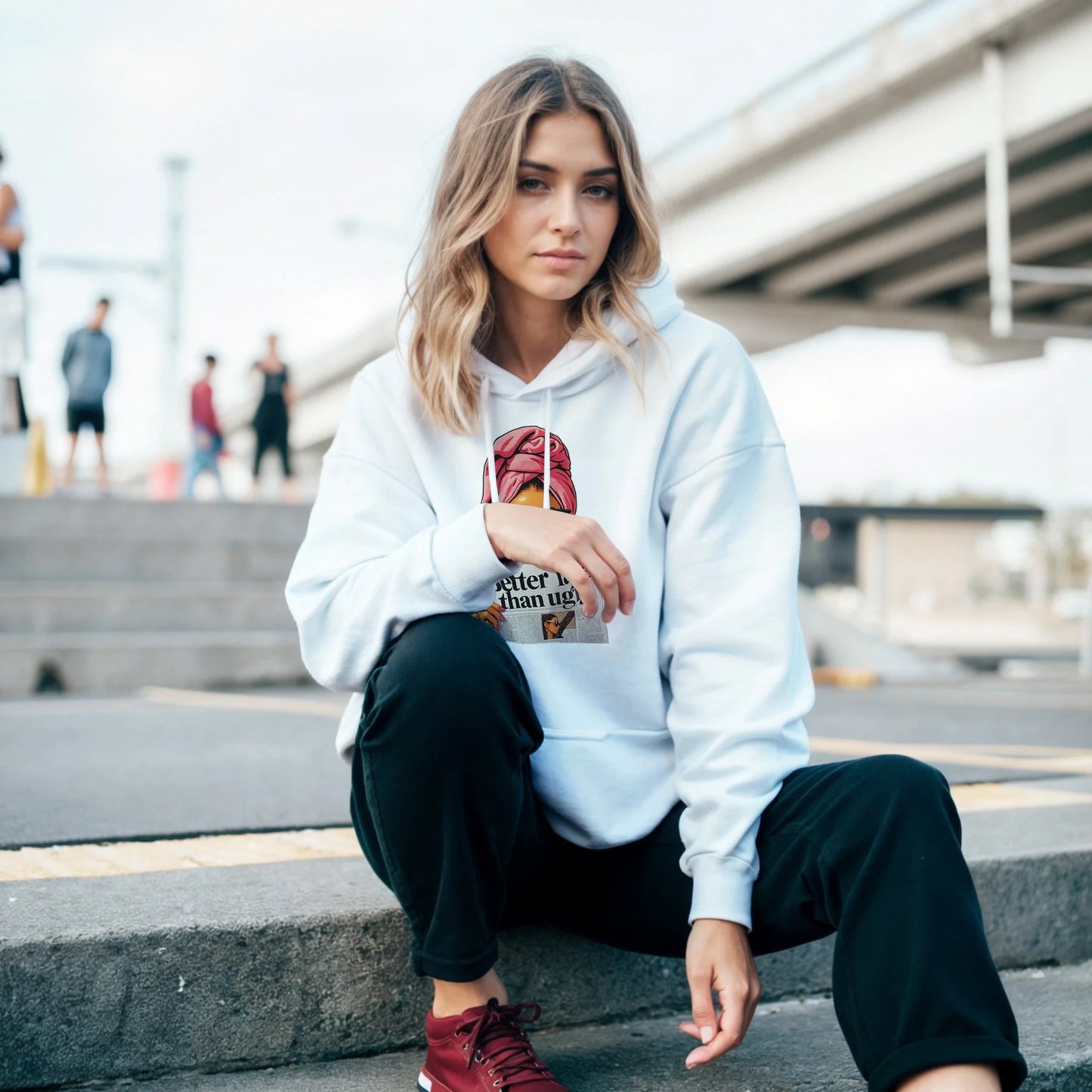Woman wearing a white hoodie with a graphic design, sitting on steps outdoors.